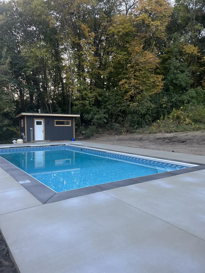 Backyard swimming pool with crystal clear water surrounded by trees and a nearby shed.