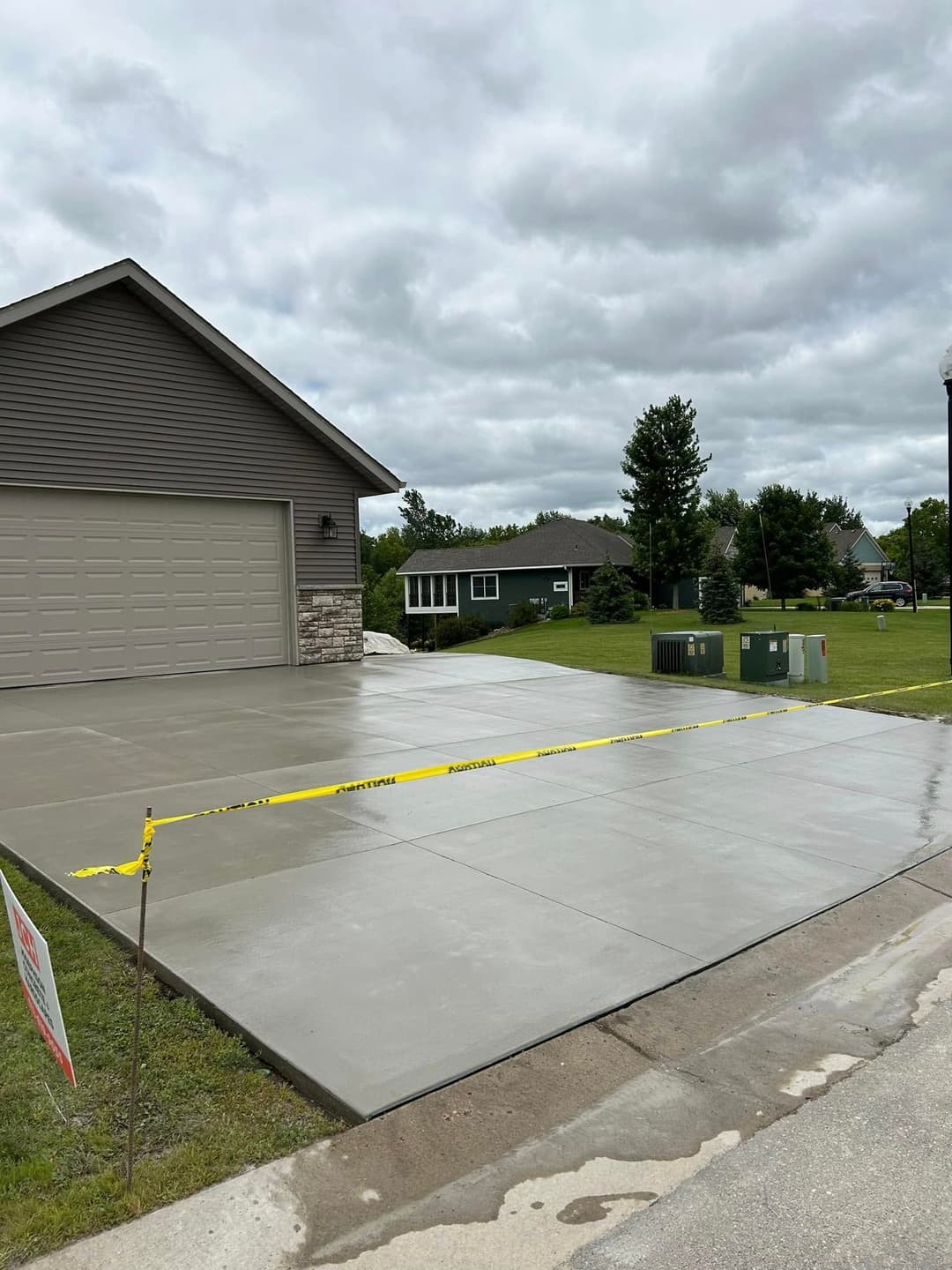 Freshly poured concrete driveway with caution tape and cloudy sky in residential area.