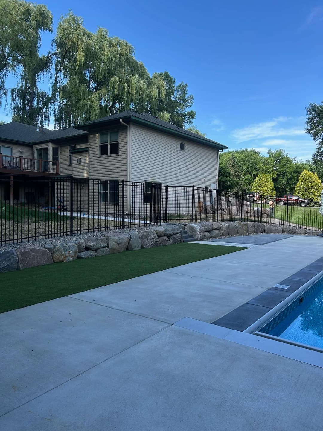Backyard view with a pool, landscaped yard, and a two-story house surrounded by a black fence.