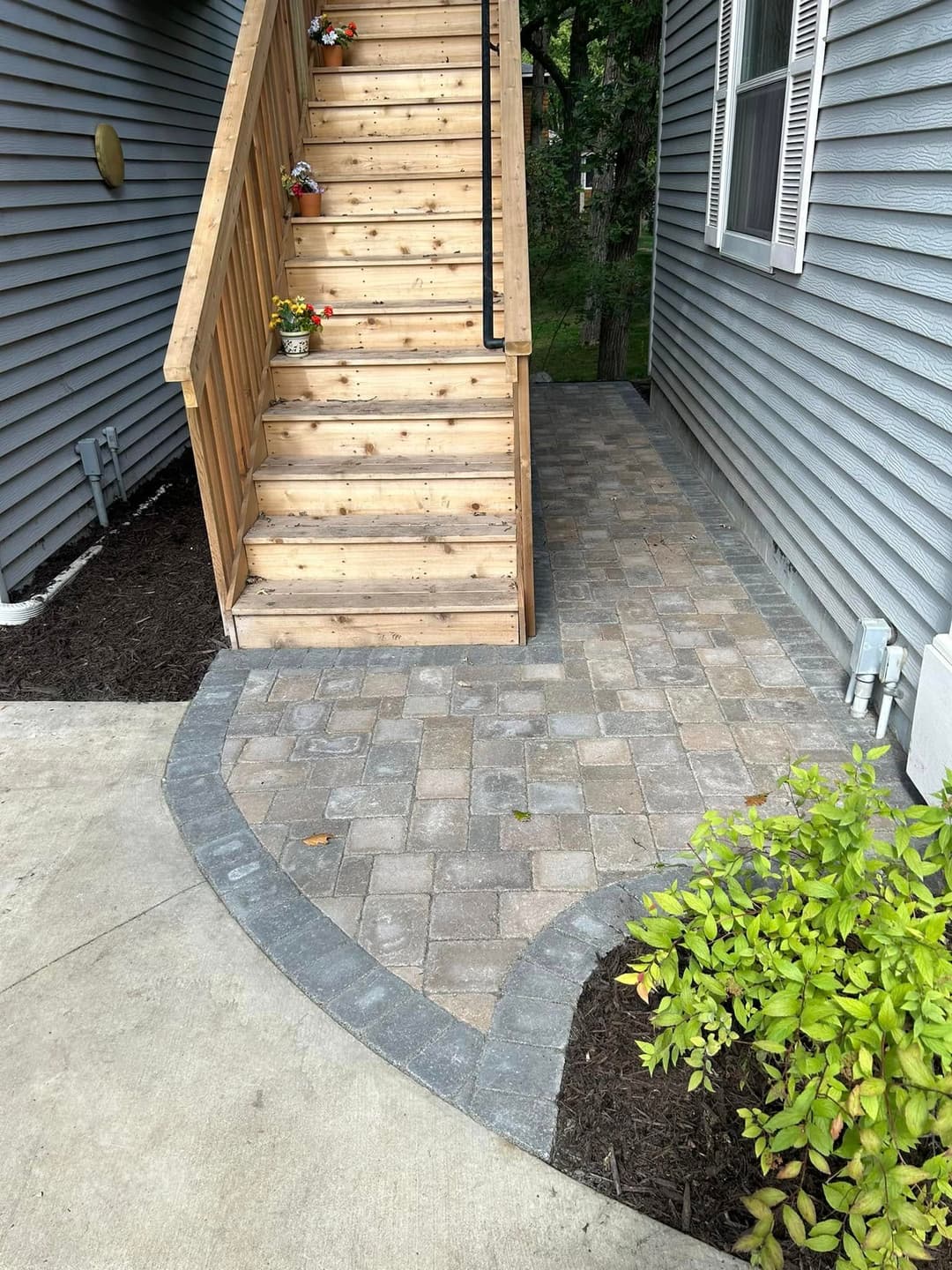 Wooden stairs leading to a brick pathway with a landscaped garden near a house.