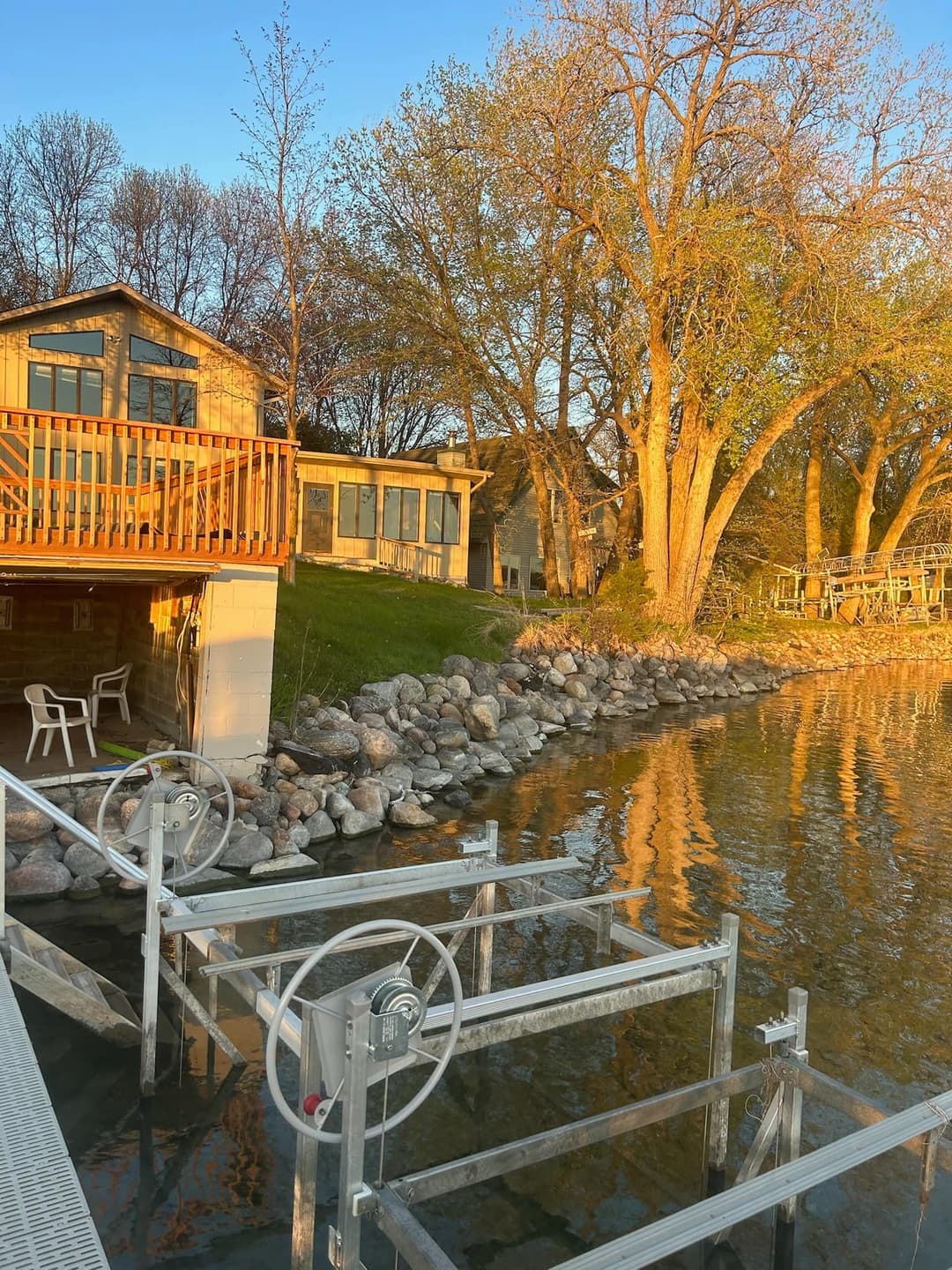 Scenic lakeside cabin at sunset with dock and trees reflecting in the water.