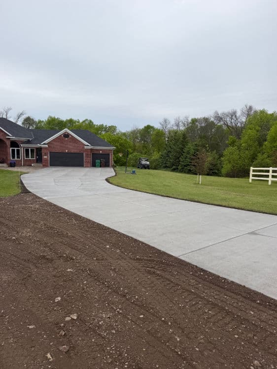 Newly poured concrete driveway leading to a brick house with green landscaping.