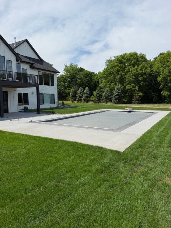 Modern home backyard with a large swimming pool and manicured lawn under a cloudy sky.