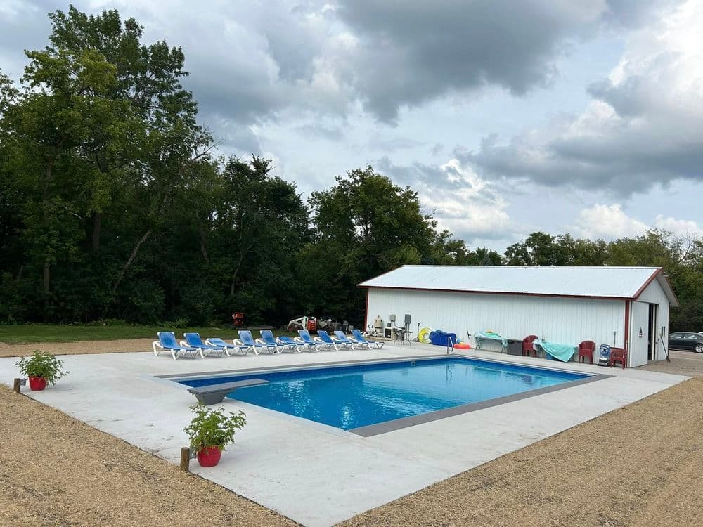 Outdoor swimming pool surrounded by lounge chairs and a storage shed, nestled in a natural setting.