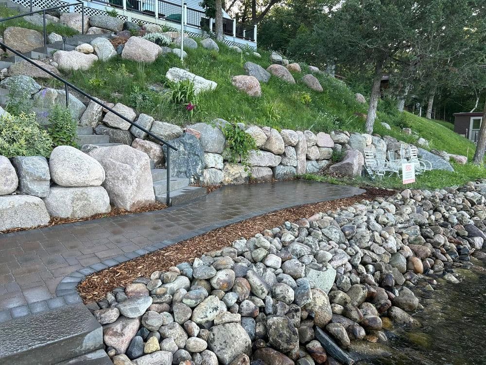 Stone pathway alongside a lakeside landscape with steps, grass, and seating area.