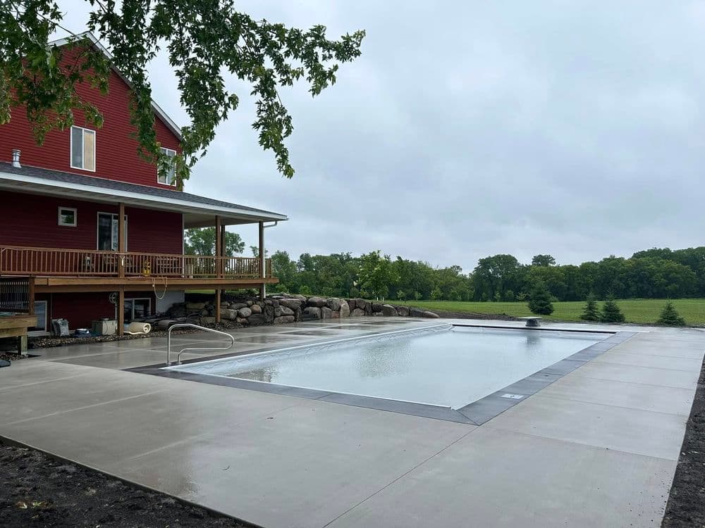 Modern home with a red exterior, featuring a rectangular swimming pool and a scenic yard.