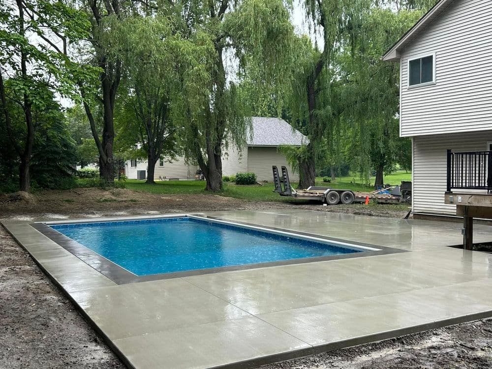 Newly constructed concrete swimming pool surrounded by lush greenery and residential homes.