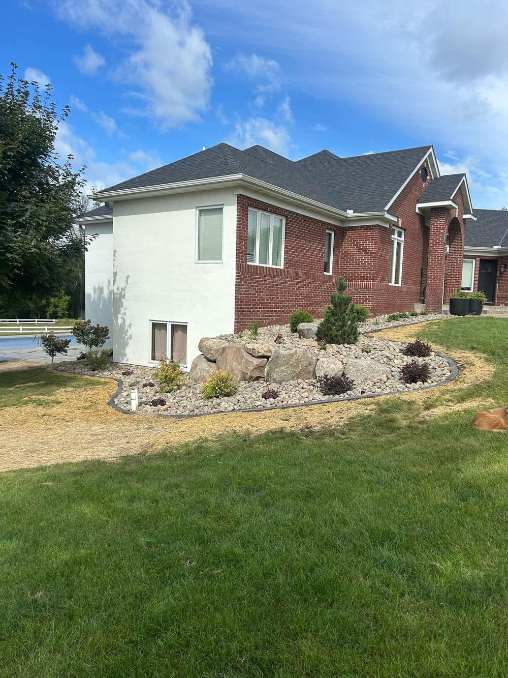 Modern brick home with landscaping, featuring rocks, shrubs, and a well-maintained lawn.