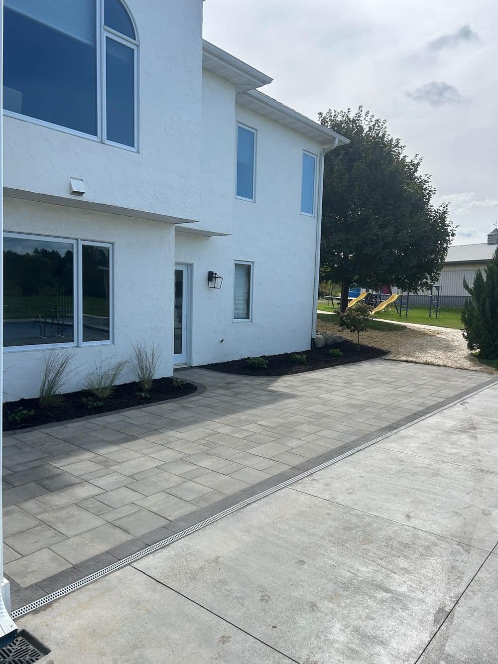 Modern home exterior with landscaped patio and nearby playground in background.