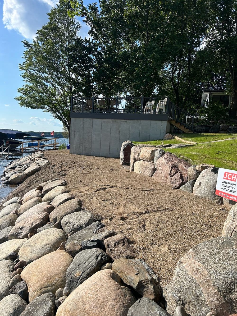 Beachfront area with rocky shoreline, trees, and a house deck overlooking the water.