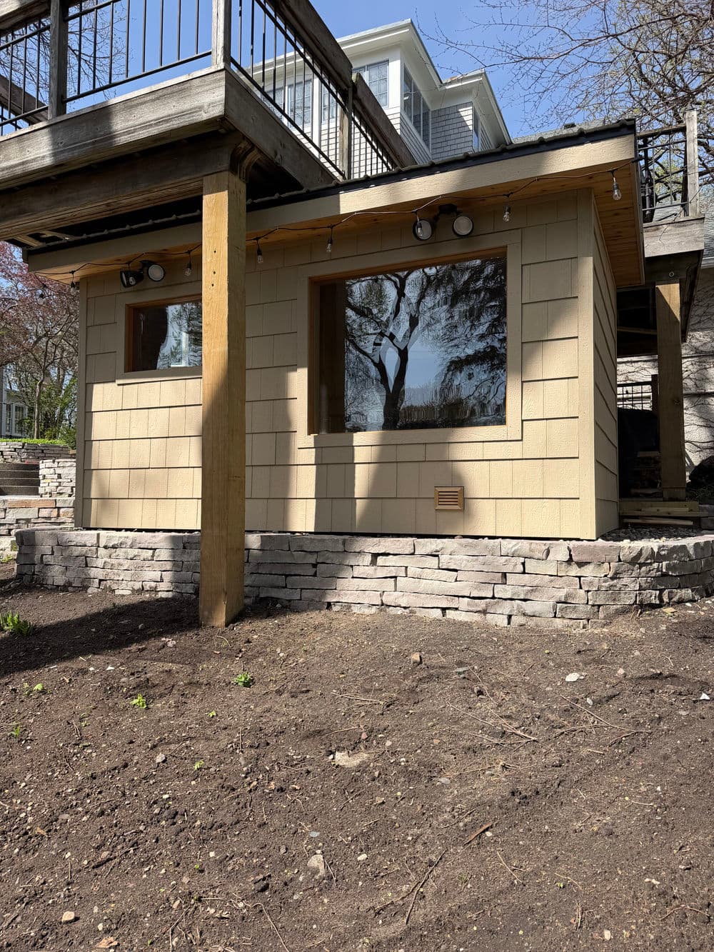 Modern garden shed with large windows and stone foundation under a wooden deck.